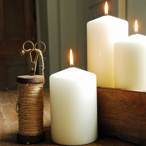 Classic ivory church pillar candles on a table next to string and scissors.