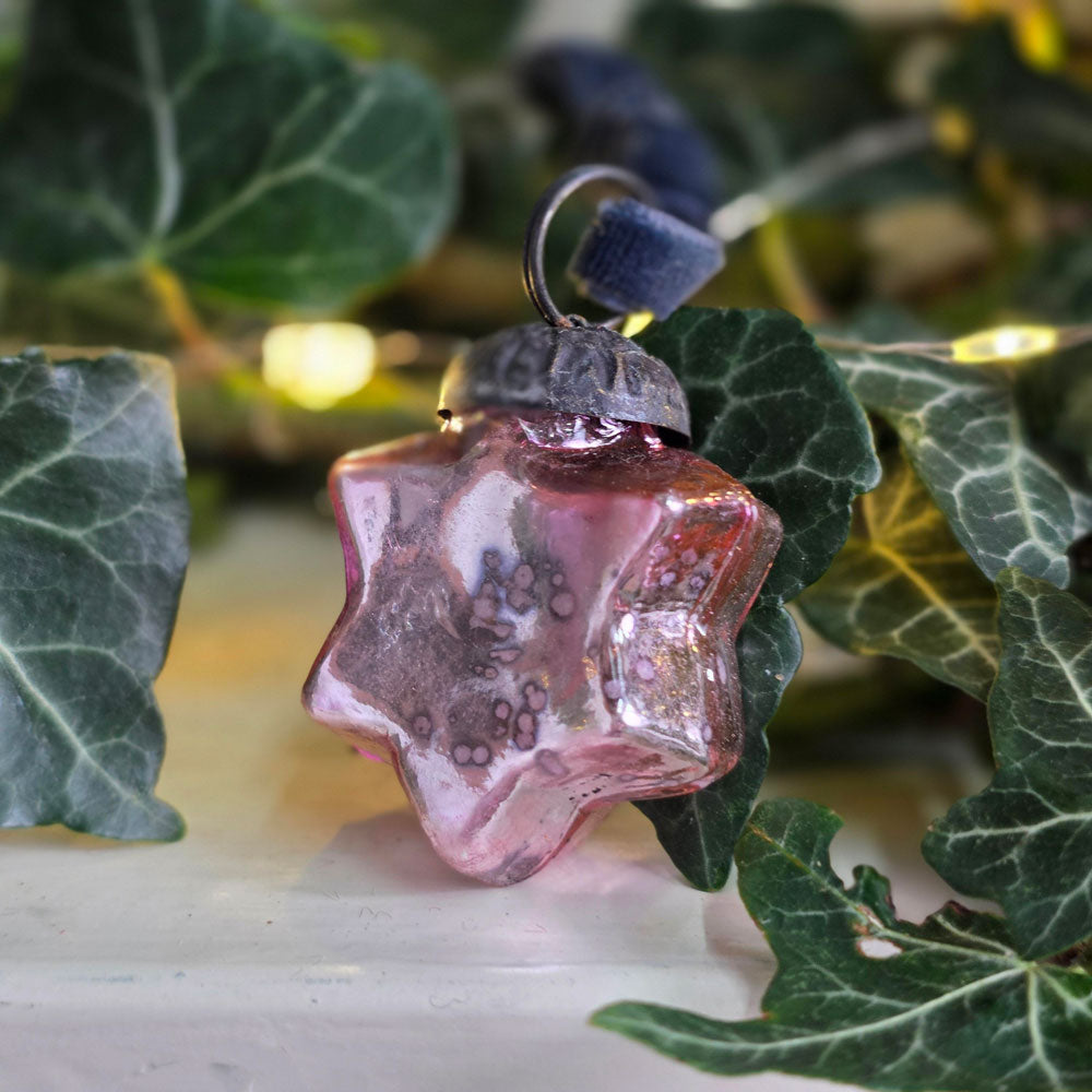 Antique style glass star tree decoration next t ivy foliage with twinkling blurred fairy lights.