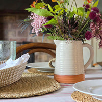 Table setting with a ceramic pitcher holding flowers on a tablecloth.