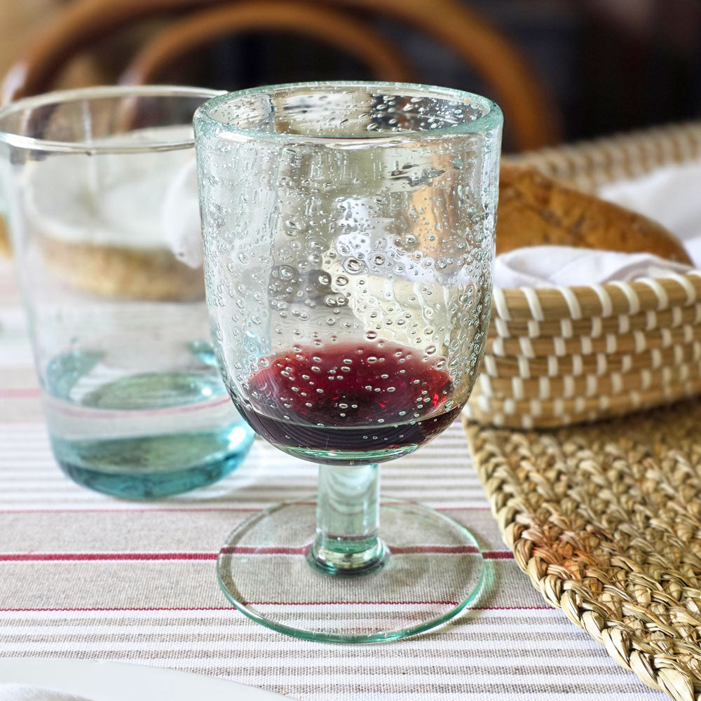 Clear glass with red liquid on a striped tablecloth with woven placemats.
