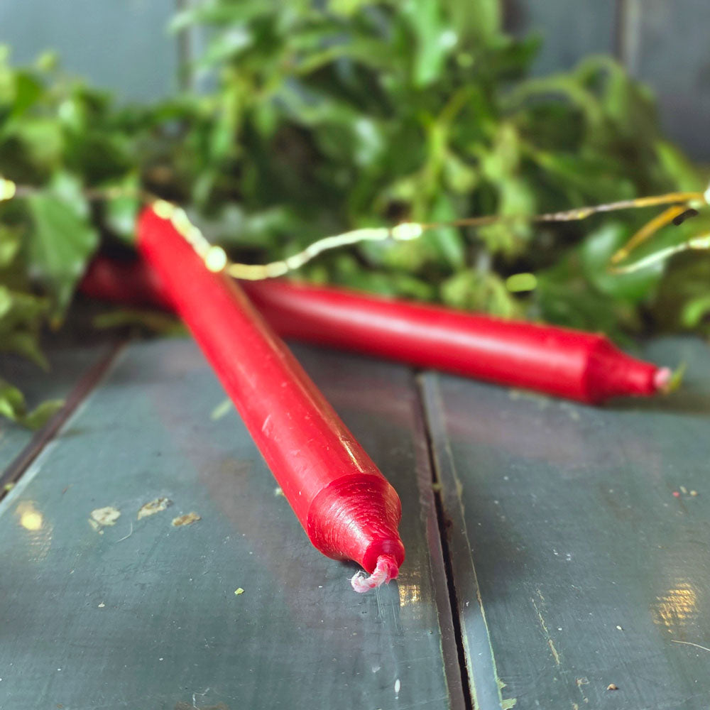 Long red dinner candles against Christmas lights and foliage.