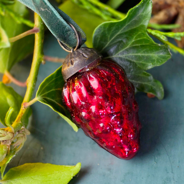 Vintage red glass bauble on blue surface with foliage.