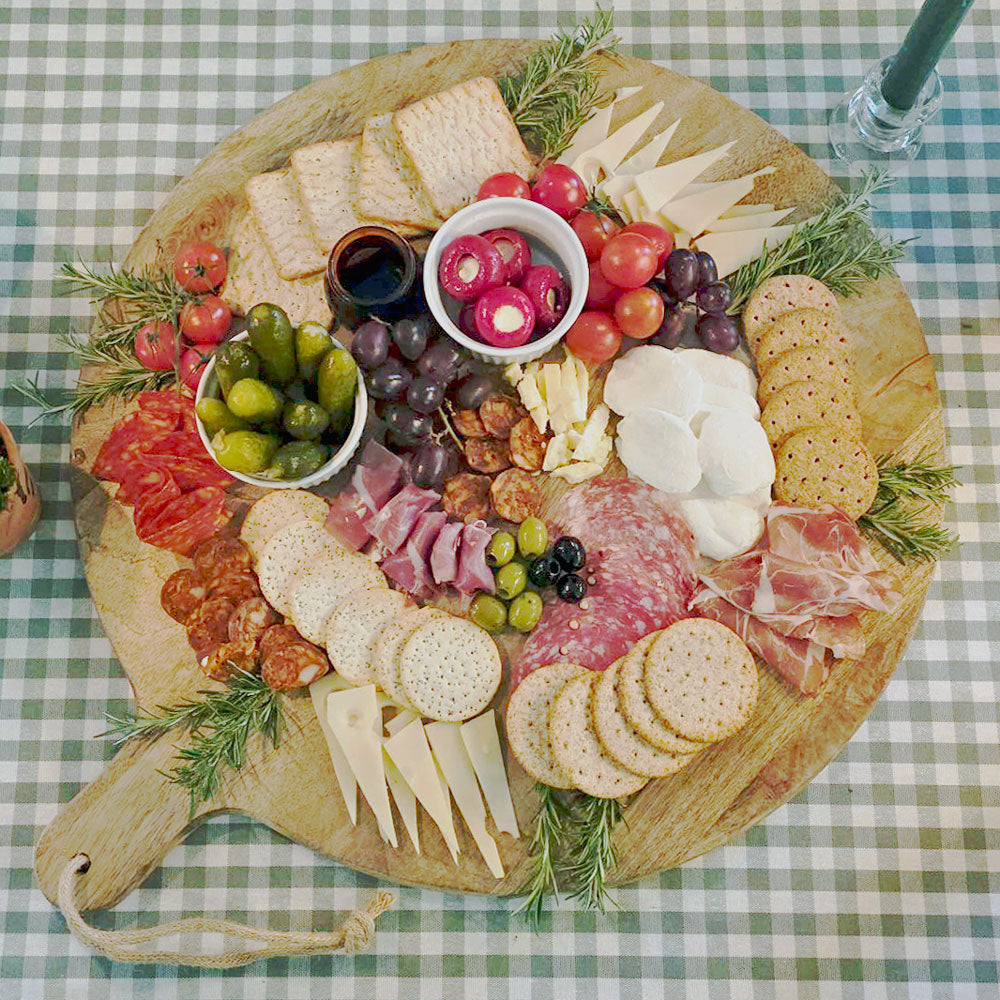 Overhead view of large round Charcuterie board on green gingham tablecloth