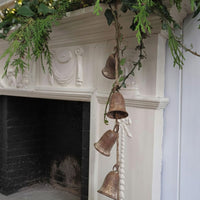  Rustic bell garland, draped over a white decorative fireplace mantel with green foliage.