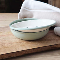 Round sage green enamel two-part soap dish on a board next to a towel