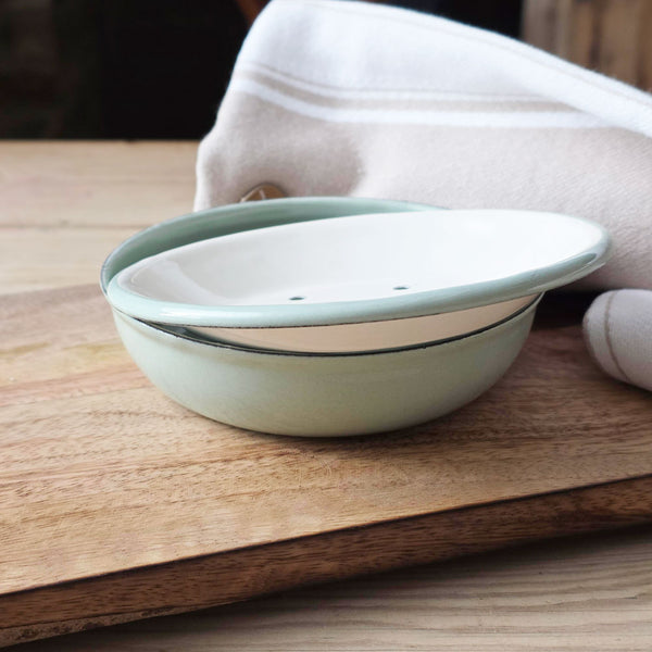 Round sage green enamel two-part soap dish on a board next to a towel