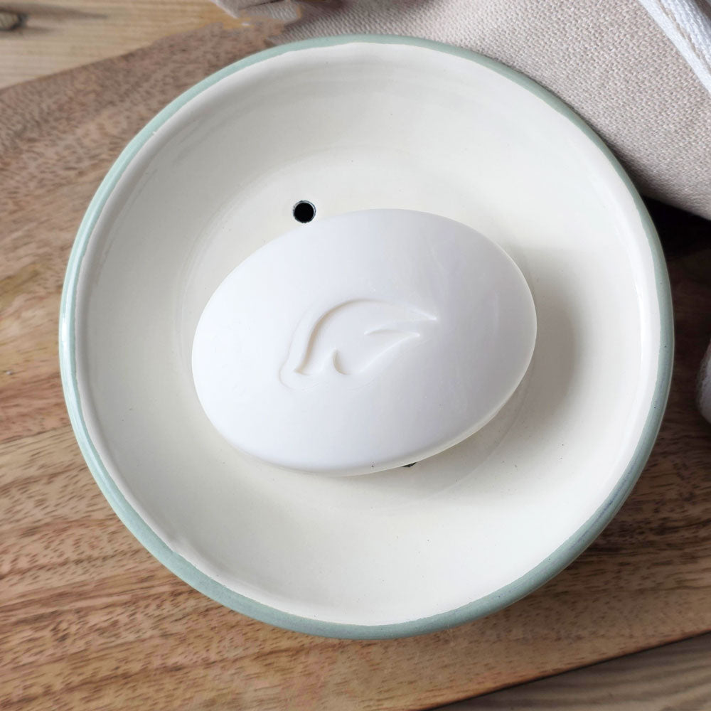 Aerial view of a white bar of soap on a round white and green enamel soap dish
