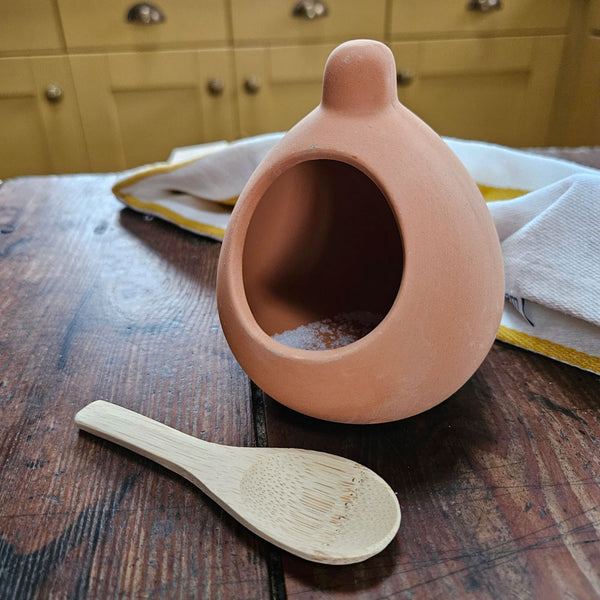 Terracotta pot and wooden spoon on a wooden surface with yellow cabinets in the background