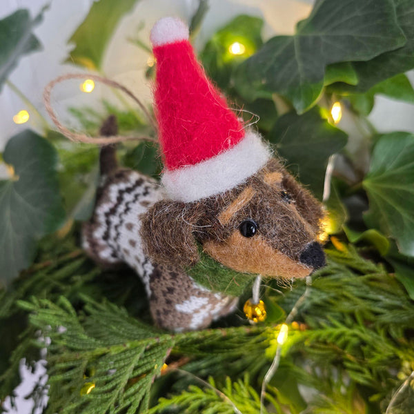 Close up of a novelty Sausage dog Christmas tree decoration surrounded by Christmas foliage and twinkling lights