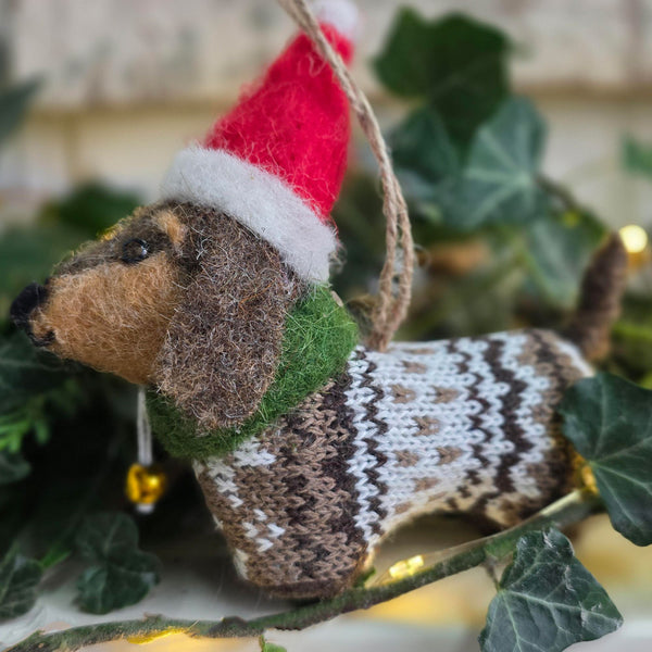 Felt Sausage dog Christmas decoration surrounded by festive foliage and ights