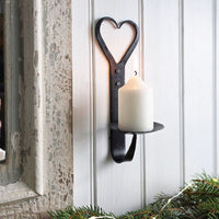 Forged iron wall mounted metal candle holder holding a small cream li candle next top a wooden frame with Christmas foliage.