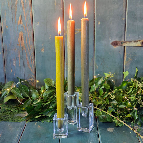 Three lit candles in clear glass holders on a rustic wooden surface with greenery.