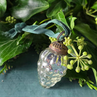 Antique silver glass grapes Christmas bauble with green velvet ribbon next to foliage.