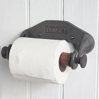 Vintage-style metal toilet paper holder with a roll of toilet paper against a white wooden panel background.