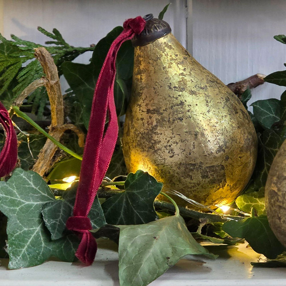 Single antique gold glass pear bauble among Ivy leaf foliage and fairy lights.