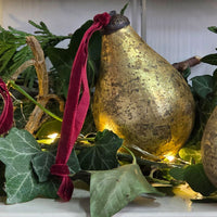 Single antique gold glass pear bauble among Ivy leaf foliage and fairy lights.