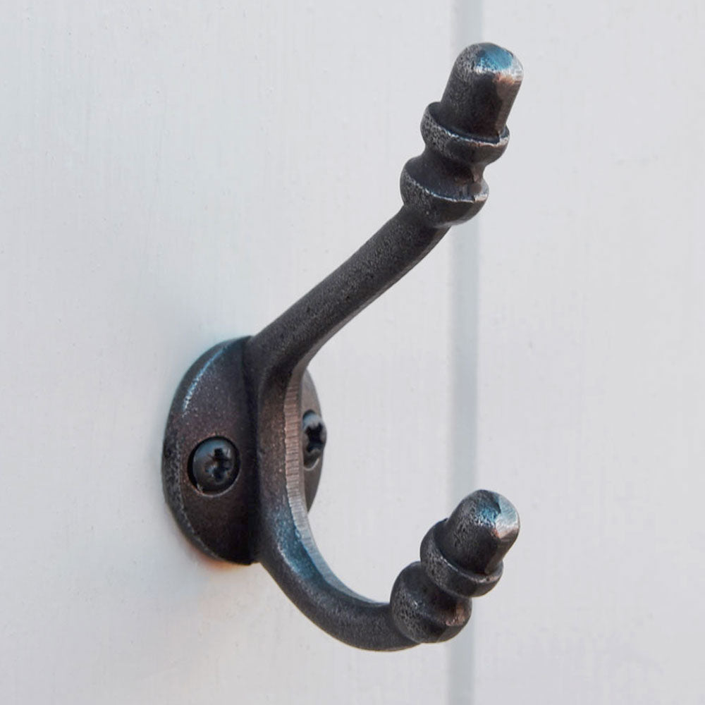 Small iron double wall hook against a white panelled wall.