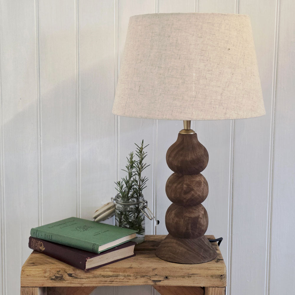 Wooden table lamp with natural linen shade on a table next to books .