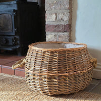 Small round wicker log basket nest to a wood burning stove.