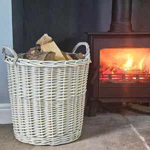 White wicker log basket filled with logs next to a lit wood burning stove.