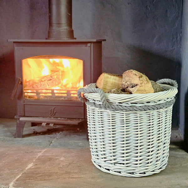 Small grey Copenhagen log basket filled with cut logs next a lit wood burning stove.