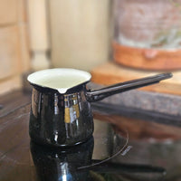 Small black enamel saucepan on a hob top.
