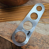 Metal spaghetti measure tool on a wooden surface with uncooked spaghetti