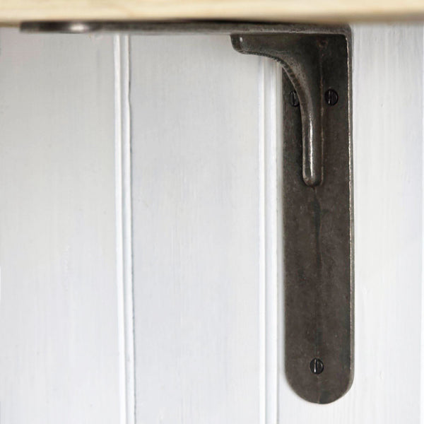 A dark metal L-bracket shelf mount shown attached to a white paneled wall, with part of a light wood shelf edge visible at the top.