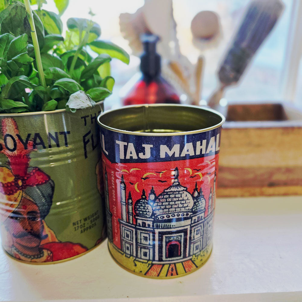Two decorative tins, one with a colorful design and 'Taj Mahal' text, the other with a face design, on a surface.