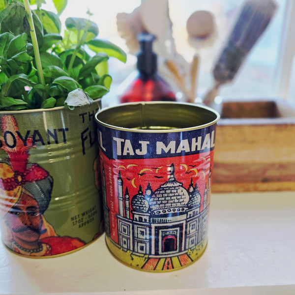 Two decorative tins, one with a colorful design and 'Taj Mahal' text, the other with a face design, on a surface.