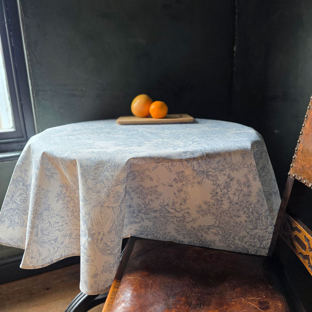 Toile de jouy wipe clean tablecloth on a round table with oranges on a board.