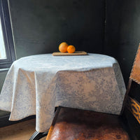 Toile de jouy wipe clean tablecloth on a round table with oranges on a board.