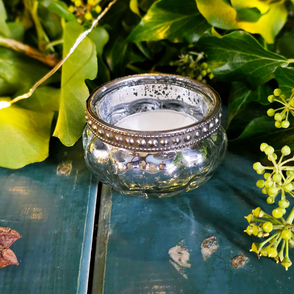 Decorative glass candle holder with a candle on a wooden surface with green leaves and flowers in the background