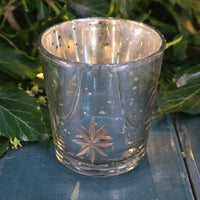 Clear glass candle holder with star design on a green surface