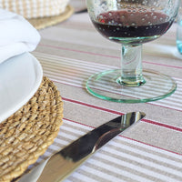 Glass of red wine, knife, and white plate on a striped tablecloth