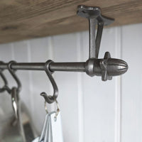 A close-up of a dark metal Highgate acorn finials and hanging hooks, mounted under a wooden shelf against a white paneled wall.