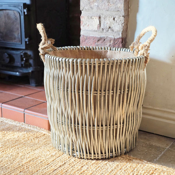 Wicker basket with handles on a stone floor next to a fireplace.