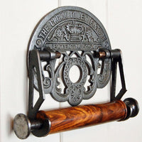 Crown cast iron toilet roll holder with wooden spindle mounted upon a painted wooden panelled wall.