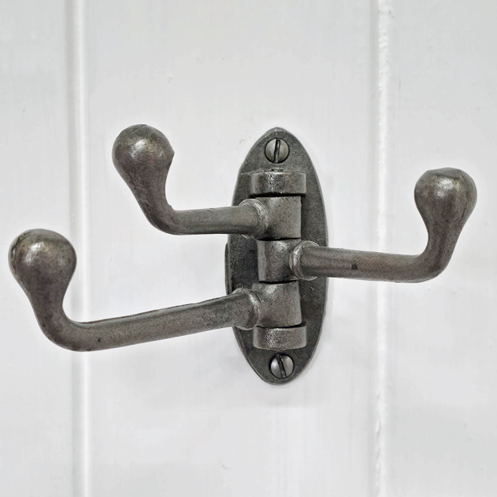 Vintage-style metal wall hook with three hooks on a white wooden panel background