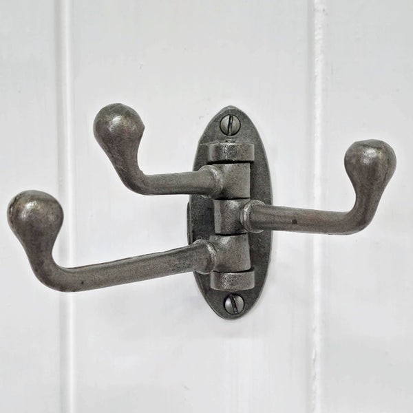 Vintage-style metal wall hook with three hooks on a white wooden panel background