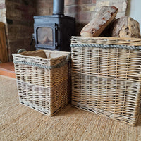 Two natural wicker storage baskets with rope handles, displayed on a textured beige rug in front of a brick fireplace and wood stove.