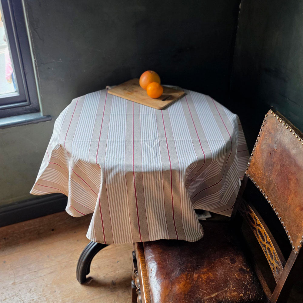 Red striped wipe clean tablecloth on a round table with oranges in a dark blue room
