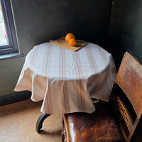 Red striped wipe clean tablecloth on a round table with oranges in a dark blue room