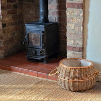 Small round log basket next to wood burning stove.
