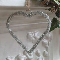 Simple silver glass beaded heart shaped decoration, hanging from a white mantelpiece.