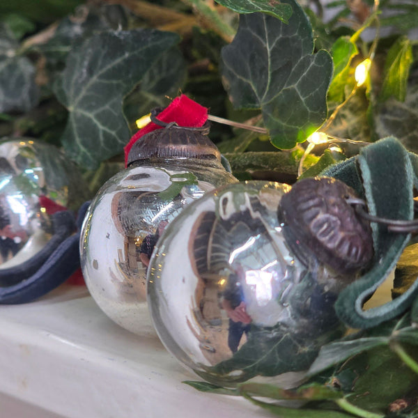 Miniature round silver Christmas baubles on a mantelpiece surrounded by ivy leaf foliage.