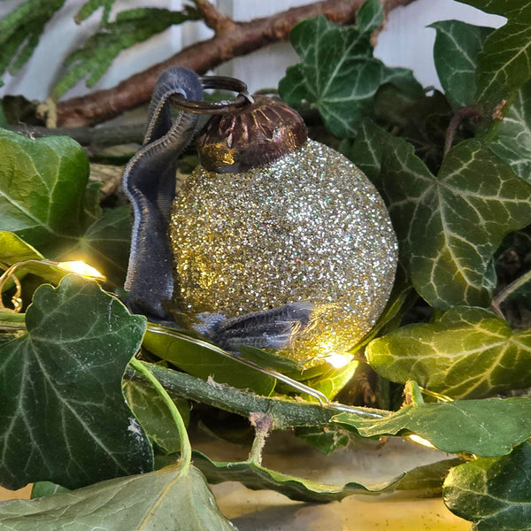 A glittery silver Christmas bauble , nestled among green ivy leaves with warm string lights.