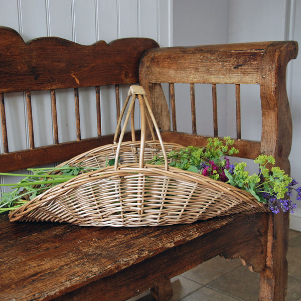 Wicker basket with flowers on an old wooden bench against a white paneled wall.
