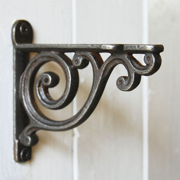 Cast iron Victorian scroll shelf bracket against a white wooden panelled wall.