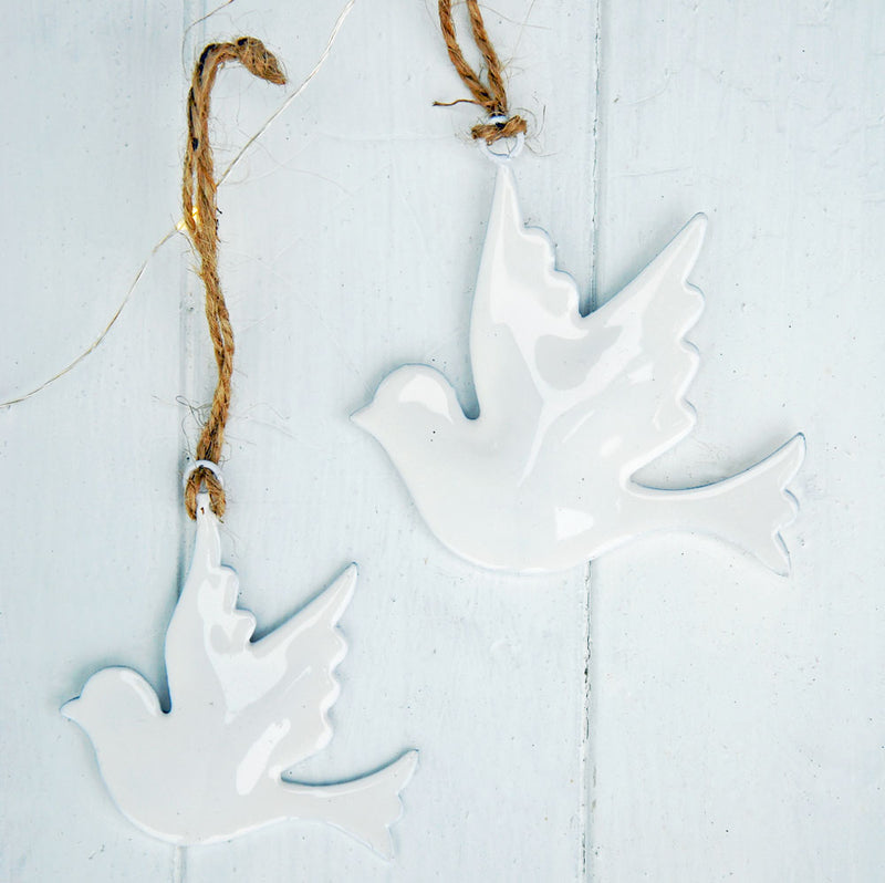 White enamel dove Christmas tree decorations photographed against a white panelled backdrop